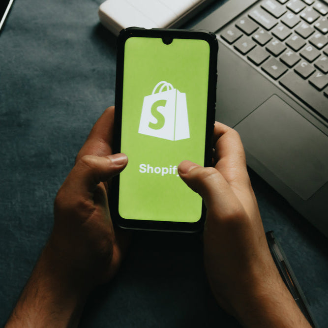 hands-holds-a-cell-phone-showing-the-shopify-logo